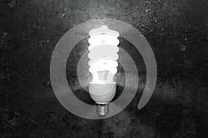 Single energy efficient light bulb glowing brightly in a dark room. New, modern, or unique energy saving idea concept