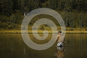 Single fisherman on a calm river is autumn fishing