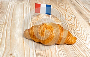 Single French Butter Croissant with Flag on Wooden Desk