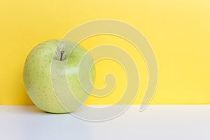 Single fresh green apple isolated on yellow background and white table. Free space for text