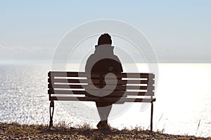 Single girl in a black jacket and hat sitting on bench at cliff at front of sea peaceful quiet place