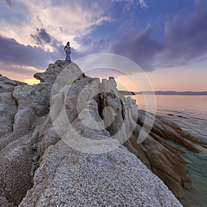 Single girl watching sunset high up on cliff by sea