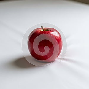 A single, glossy red apple rests on a white surface, casting a soft shadow