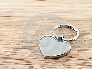 single glossy silver metallic heart shaped key chain on wooden desk floor