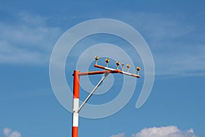 Single high metal red and white pole with multiple airport runway guiding lights on cloudy blue sky