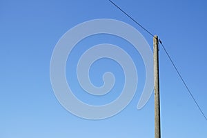 A single high voltage power line against blue cloudless sky. Overhead line on a wood pylon