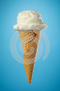 Single ice cream cone with vanilla icecream and a waffle cone on blue background