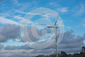 Single large white wind turbine with cloudy blue sky background