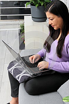 Single Latin adult woman uses her laptop on the couch at home to do home office, shop online, make video calls, make romantic date