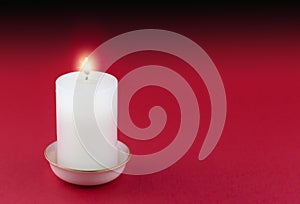 Single lit candle in gold rimmed white holder on red