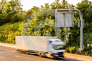 Single lorry truck on uk motorway road under information display at sunset