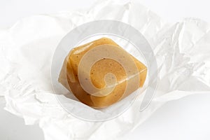 SIngle luxury unwrapped caramel toffee on white wrapper in perspective.