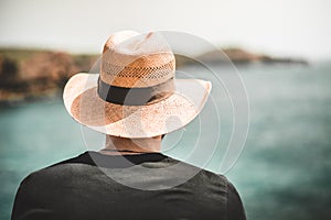 Single male with hat looking into the distance with water and cliffs