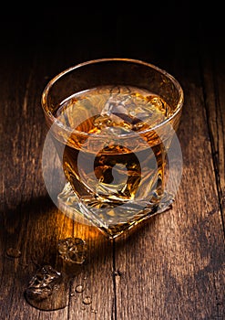 Single malt scotch whiskey in modern crystal glass with ice cubes on wooden background