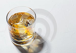 Single malt whiskey in glass with ice cubes with shadow on white