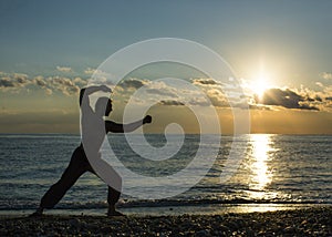Single man does martial arts on the beach during sunset time. Wushu.