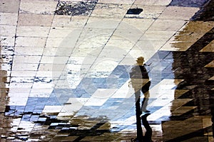 Single man reflection silhouette on wet sidewalk