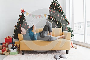 A single man seems lonely using his phone and lay down on sofa in living room decorated with Christmas tree