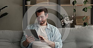 Single man sit on sofa holding tablet enjoy e-date services