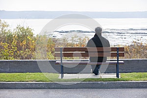 Single mature man sitting on park bench overlooking River in Autumn.