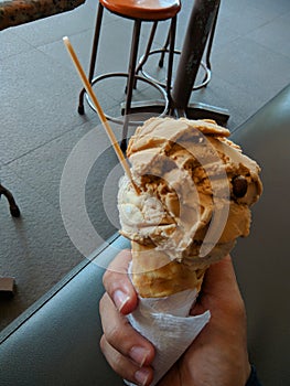 Single melting brown chocolate ice cream scoop flavor in waffle cone in hand holding