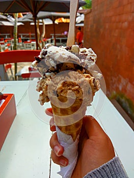 Single melting brown chocolate ice cream scoop flavor in waffle cone in hand holding