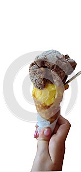 Single melting chocolate and yellow ice cream scoop flavor in waffle cone in hand holding on white