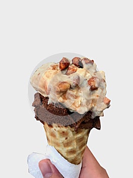 Single melting vanilla and chocolate ice cream scoop flavor in waffle cone in hand holding on white