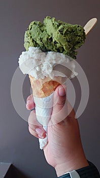 Single melting vanilla ice cream scoop flavor in waffle cone in hand holding