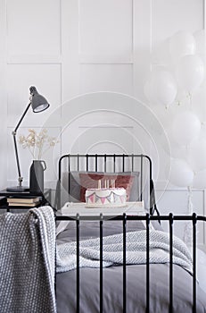 Single metal bed with grey bedding and burgundy pillow, birthday cake with candles on white trey, real photo with