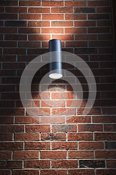 Single metal lamp illuminating a blank red brick wall