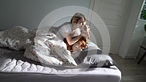 Single middle-aged woman playing and cuddling with beloved dog in bed after waking up