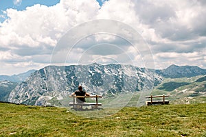 Single millenial man sits on a bench on a mountain plateau and looks at the mountains in front of him. Montenegro, Durmitor