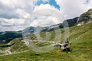 Single millenial man sits on a bench on a mountain plateau and looks at the mountains in front of him. Montenegro, Durmitor.