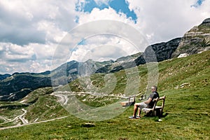 Single millenial man sits on a bench on a mountain plateau and looks at the mountains in front of him. Montenegro, Durmitor.