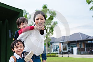 Single mom carrying and playing with her children in  garden with green wall background. People and Lifestyles concept. Happy