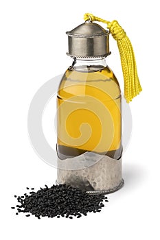 Single Moroccan bottle with Nigella oil and a heap of nigella seed on white background close up