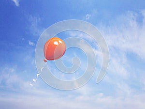 Single orange balloon in the blue sky