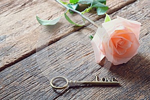 Single orange-pink rose and Love key shape on vintage wooden floor under soft warm light. Backdrop for Valentine's day