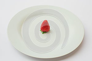 Single organic and fresh strawberry on a white plate.