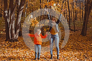 Single parent family playing with autumn leaves in park. Happy mom and son throw autumn leaves up in fall park.