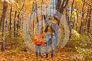 Single parent family playing with autumn leaves in park. Happy mom and son throw autumn leaves up in fall park.