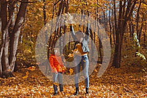 Single parent family playing with autumn leaves in park. Happy mom and son throw autumn leaves up in fall park.