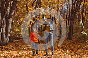 Single parent family playing with autumn leaves in park. Happy mom and son throw autumn leaves up in fall park.