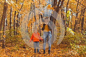 Single parent family playing with autumn leaves in park. Happy mom and son throw autumn leaves up in fall park.