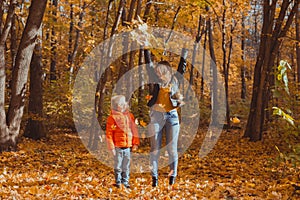 Single parent family playing with autumn leaves in park. Happy mom and son throw autumn leaves up in fall park.