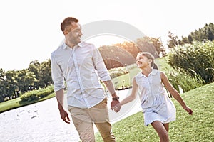 Single parent, Father and daughter walking on a grassy field hol