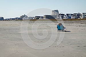 A single person sitting on a beach chair on a wide empty sandy beach