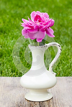 Single pink peony flower in white ceramic vase