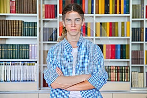 Single portrait of serious confident male student teenager looking at camera in library